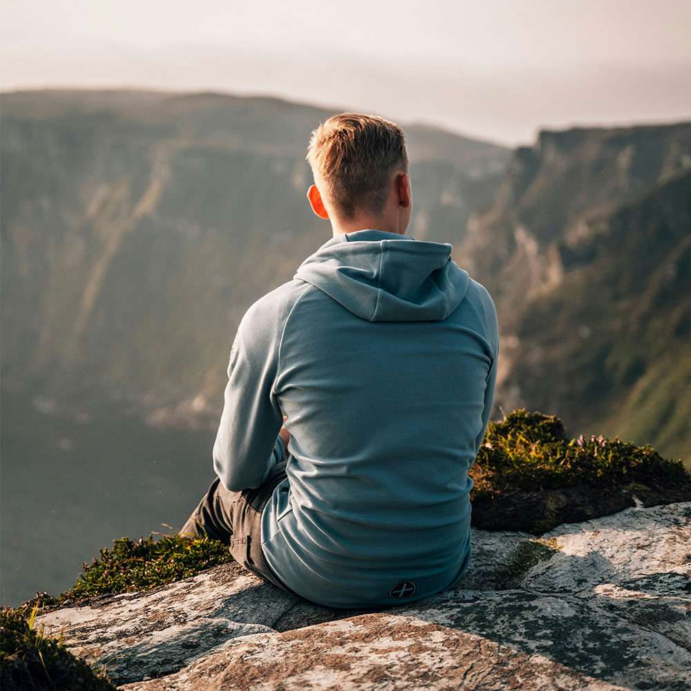 Man sitting on a ledge, looking at a view of mountains