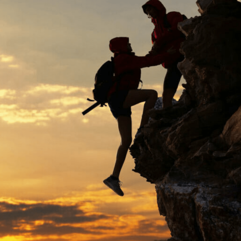A hiker person helping someone up over a ridge