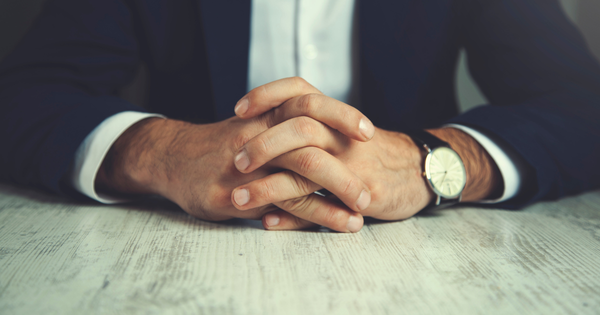 A man in a suit crossing his hands on a table